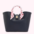 Navy blue tote bag with a white silk scarf adorned with red lips printed on it around the handle.