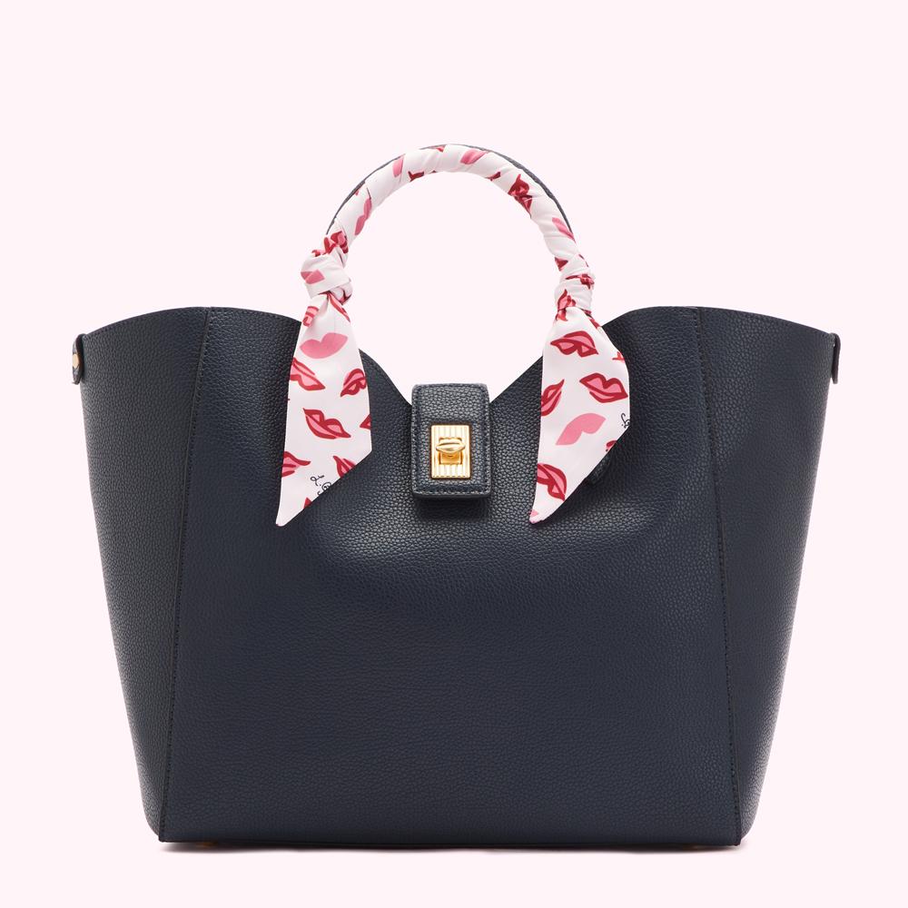 Navy blue tote bag with a white silk scarf adorned with red lips printed on it around the handle.